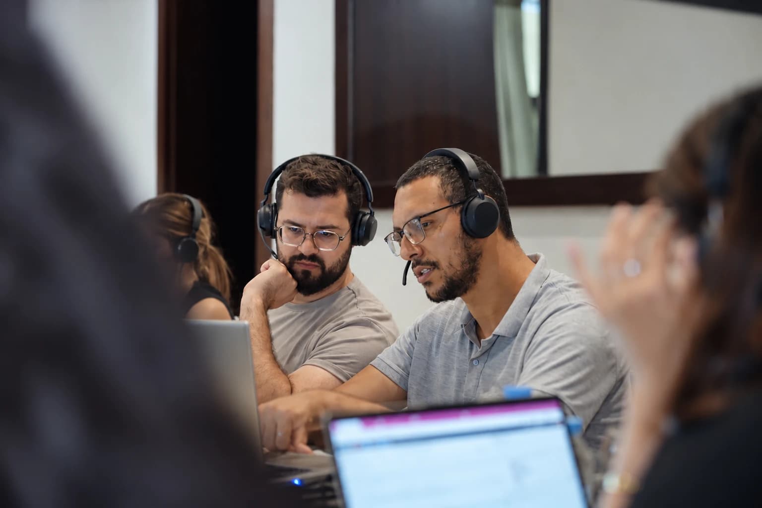 A TCrew consultant with a headset explaining his screen to a colleague during a working session